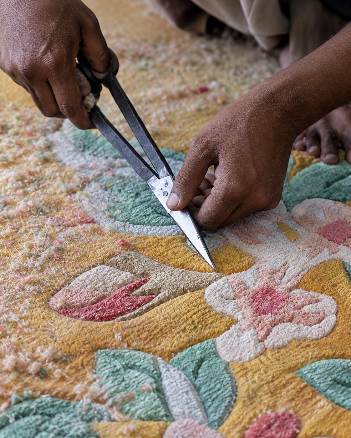 An artisan hand-trimming the pile of a floral hand-tufted rug